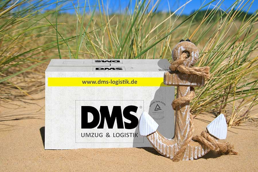 Umzugskarton auf Strand neben Anker